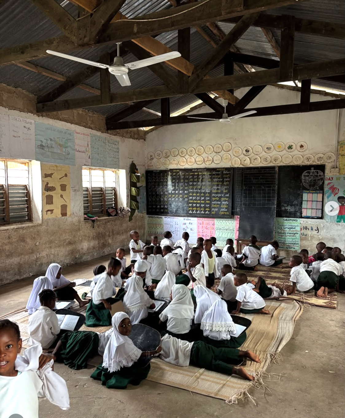 Students sitting on mats in a large classroom in Zanzibar